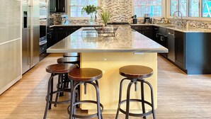 A modern kitchen with a large island, bar stools, and a hanging light fixture.