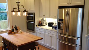 A modern kitchen with white cabinets, stainless steel appliances, and a wooden table with bar stools. - Walk to AVL's TOP restaurants, pubs, etc. Ashehville’s historic Falconhurst area (Asheville)