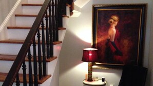A staircase with wooden steps and black balusters, a chandelier, a framed painting on the wall, and a table lamp with a red shade. - Walk to AVL's TOP restaurants, pubs, etc. Ashehville’s historic Falconhurst area (Asheville)