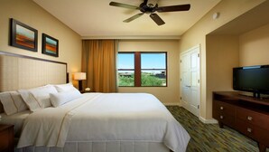 Ein Hotelzimmer mit Bett, Fernseher, Deckenventilator, Fenster mit Blick und Bildern an der Wand.