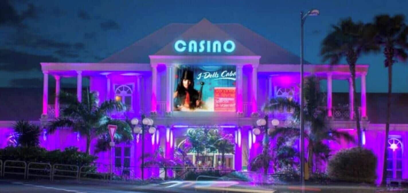 A casino building with a neon sign, palm trees, and a large illuminated window.