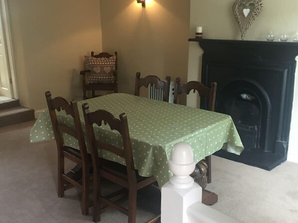 A dining room with a table set for four, surrounded by wooden chairs, a fireplace, and a patterned chair in the corner. - Beautiful Stone Cottage in Wensleydale (Hunton, Bedale)