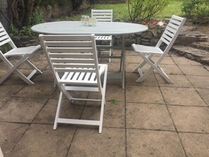 A round patio table with four white chairs, a small table with condiments, and a stone wall in the background. - Beautiful Stone Cottage in Wensleydale (Hunton, Bedale)