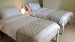 Two single beds with white bedding and a nightstand with a lamp. - Beautiful Stone Cottage in Wensleydale (Hunton, Bedale)