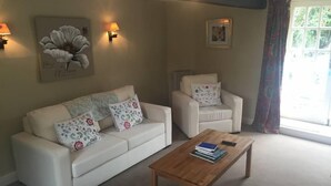A living room with a sofa, armchair, and coffee table. There are wall-mounted lamps, a framed picture, and a window with curtains. - Beautiful Stone Cottage in Wensleydale (Hunton, Bedale)
