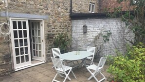 A stone building with a patio area featuring a round table and white chairs. - Beautiful Stone Cottage in Wensleydale (Hunton, Bedale)