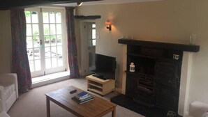 A living room with a fireplace, a television on a wooden stand, a sofa, and a coffee table. - Beautiful Stone Cottage in Wensleydale (Hunton, Bedale)