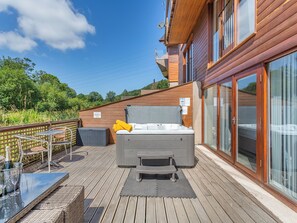 Eine Holzterrasse mit Whirlpool, Tisch und Stühlen sowie einem Glasgeländer.