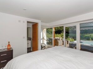 Ein Schlafzimmer mit einem großen Bett, einem Schminktisch und Blick auf einen Außenbereich mit einem Whirlpool.