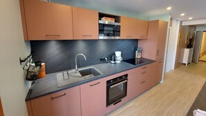 Eine moderne Küche mit rosa Schränken, einer schwarzen Arbeitsplatte, einer Edelstahl-Mikrowelle und einem eingebauten Ofen.