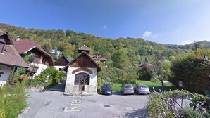 Ein ländliches Dorf mit traditionellen Holzhäusern, einem steinernen Eingangstor und geparkten Autos.