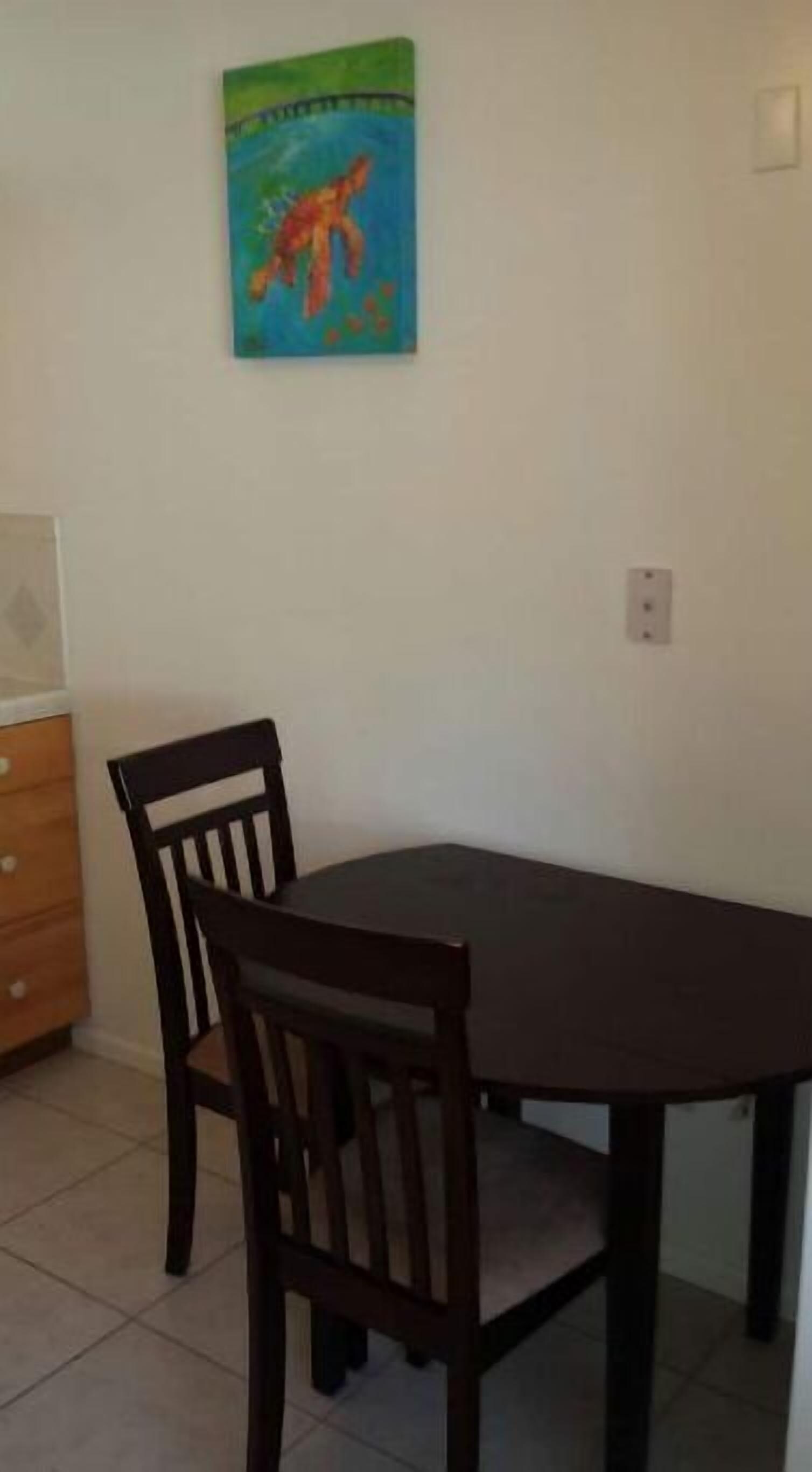 Een eetruimte met een donker houten tafel en twee stoelen. Daarboven hangt een kleurrijk schilderij aan de muur.