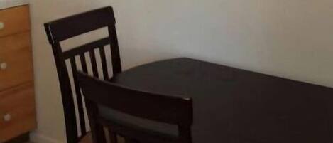 Een eetruimte met een donker houten tafel en twee stoelen. Daarboven hangt een kleurrijk schilderij aan de muur.