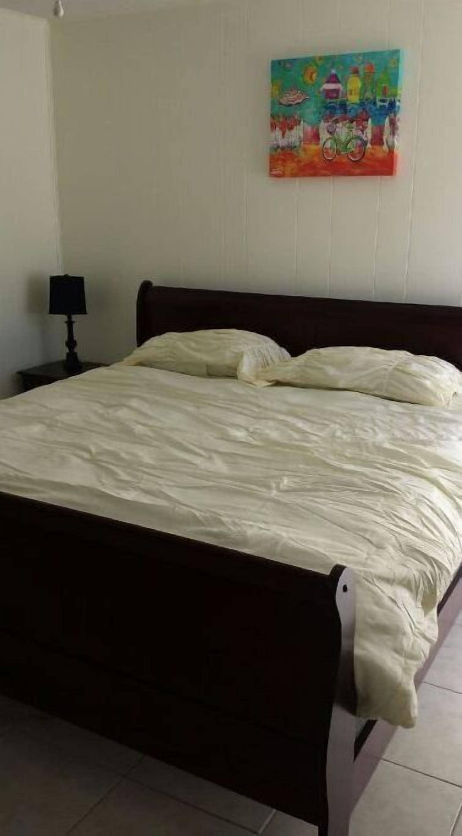 Un dormitorio con una cama, una mesita de noche y un cuadro de colores en la pared.