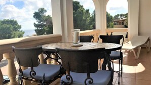 A covered outdoor seating area with a round table and chairs, overlooking a scenic view. - quality furnishings, large pool, stunning sea views, just 200m to the beach (Cala Santanyí)