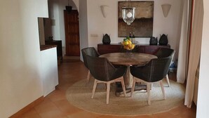 A dining area with a round wooden table, four wicker chairs, a woven rug, and a painting above the table. - quality furnishings, large pool, stunning sea views, just 200m to the beach (Cala Santanyí)