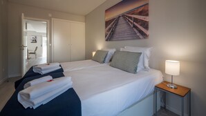 A hotel room with two beds, a painting of a beach, a bedside lamp, and a view of the hallway.