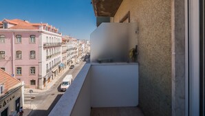 A balcony with a view of a street lined with buildings, a clear sky, and a parked van.
