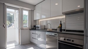 A modern kitchen with white cabinetry, stainless steel appliances, and a view of a green landscape through a large window.