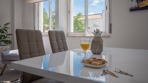 A modern dining area with a white table, two chairs, a glass of orange juice, a plate of pastries, and keys on the table.