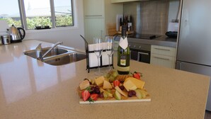 A kitchen with a marble countertop, a wine bottle, glasses, and a cheese platter. - Stunning Views Over Tokerau Beach (Karikari Peninsula)
