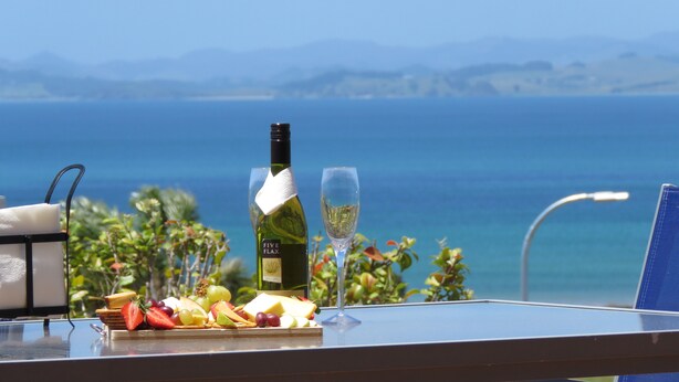 A table with a bottle of wine, a glass, and a fruit platter. - Stunning Views Over Tokerau Beach (Karikari Peninsula)