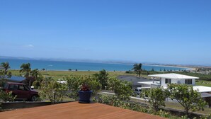 A residential area with a view of the ocean, a white house, and a red car parked on a wooden deck. - Stunning Views Over Tokerau Beach (Karikari Peninsula)