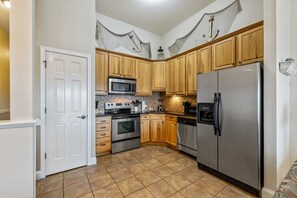 A kitchen with wooden cabinets, stainless steel appliances, and a tiled floor. - FFR302  The Starboard by First Flight Rentals (Kill Devil Hills)