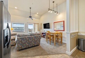 A living room with a sofa, a dining table with chairs, a ceiling fan, and a view of the outside. - FFR302  The Starboard by First Flight Rentals (Kill Devil Hills)