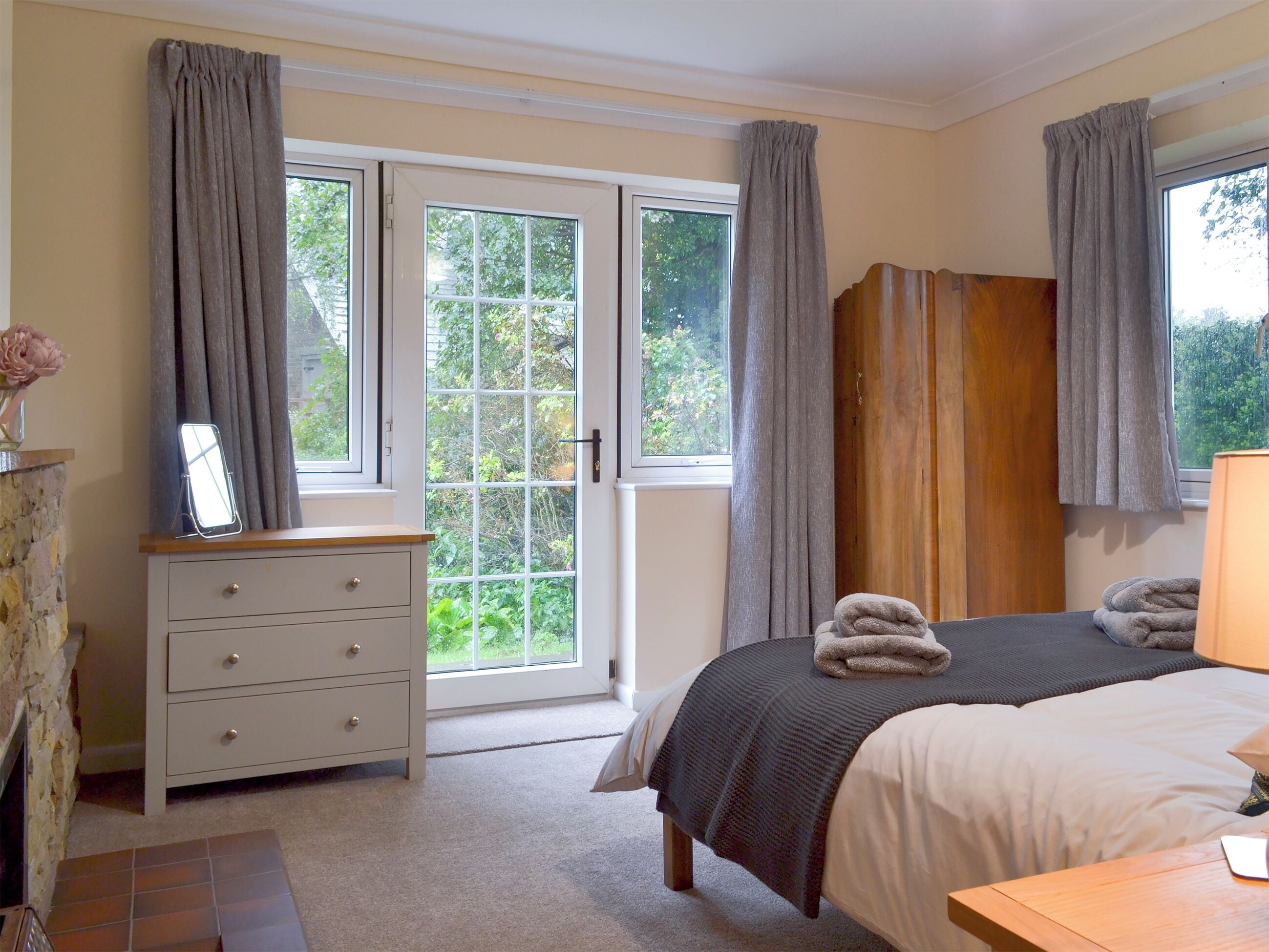 Een slaapkamer met een bed, een dressoir, een spiegel en een raam met gordijnen.