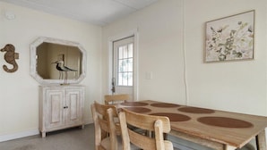 A dining area with a wooden table and chairs, a white cabinet, a mirror, and a framed floral artwork on the wall.