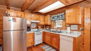 A wooden cabin kitchen with a stainless steel refrigerator, white stove, and wooden cabinets. - Cute, Cozy Cabin for a Romantic Getaway! Pool, Putt Putt, Fishing, Golf, Tennis (Sevierville)