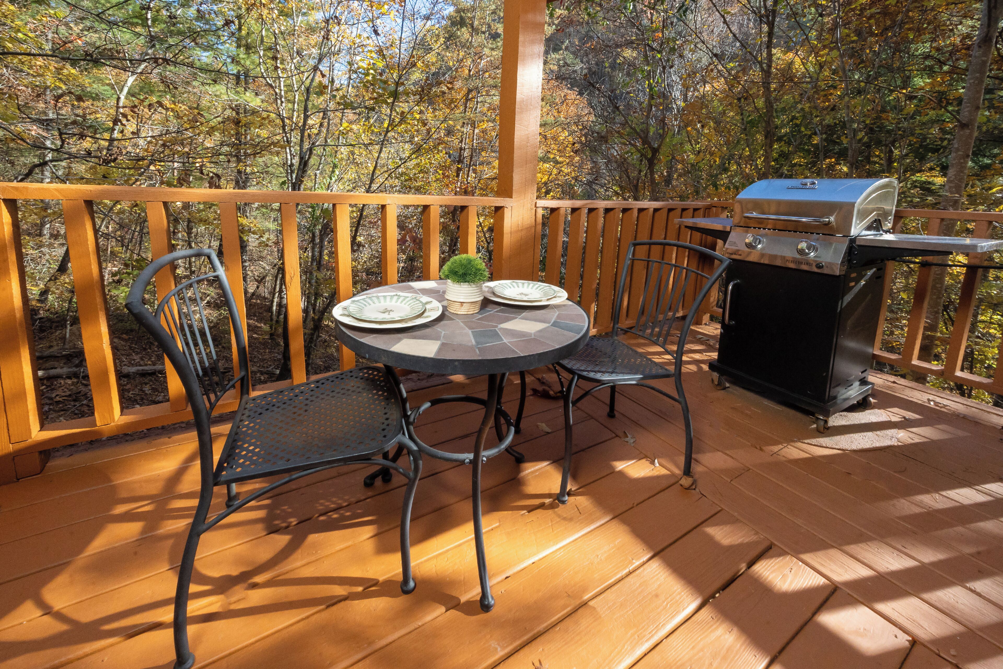 A wooden deck with a table and chairs, a grill, and a view of trees.