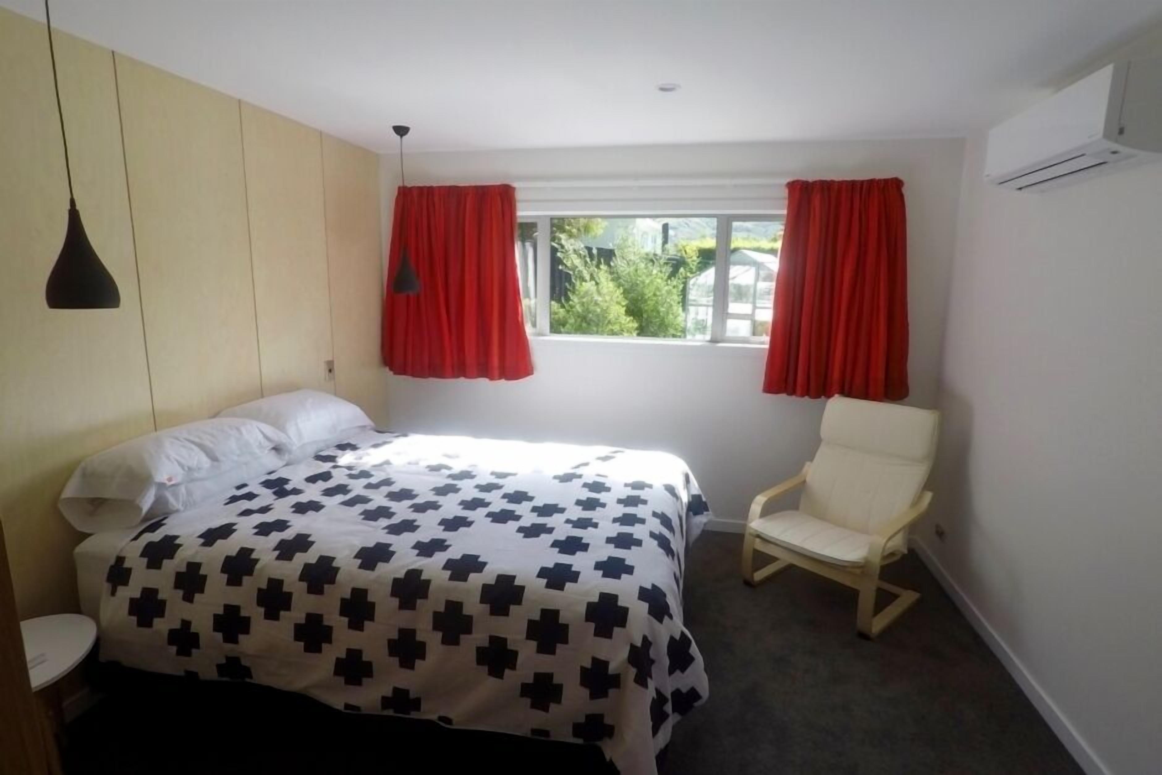 Una camera da letto con un letto, una sedia, una finestra con tende e un condizionatore d'aria.