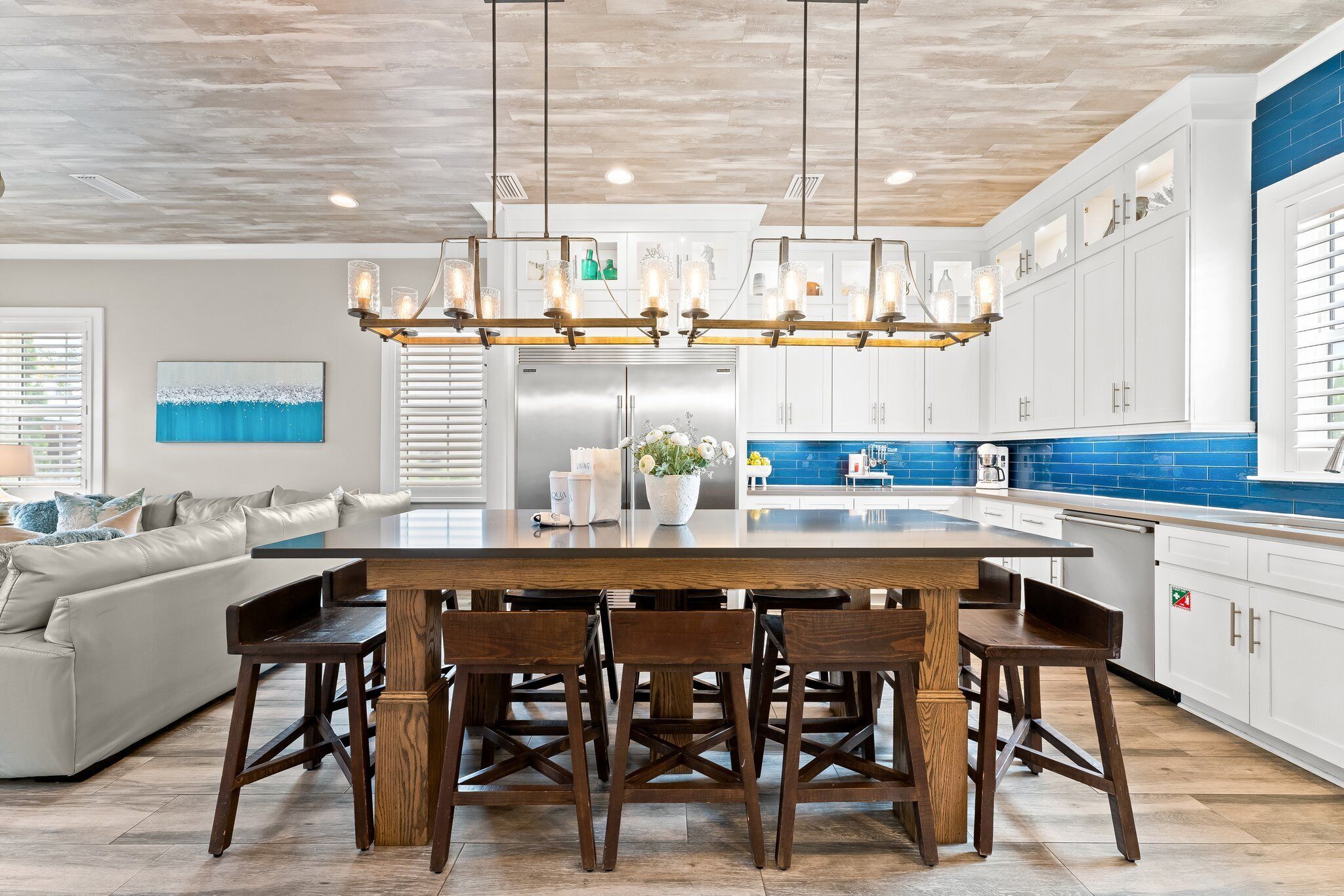 A modern kitchen with a central island, white cabinets, blue backsplash, and a chandelier.