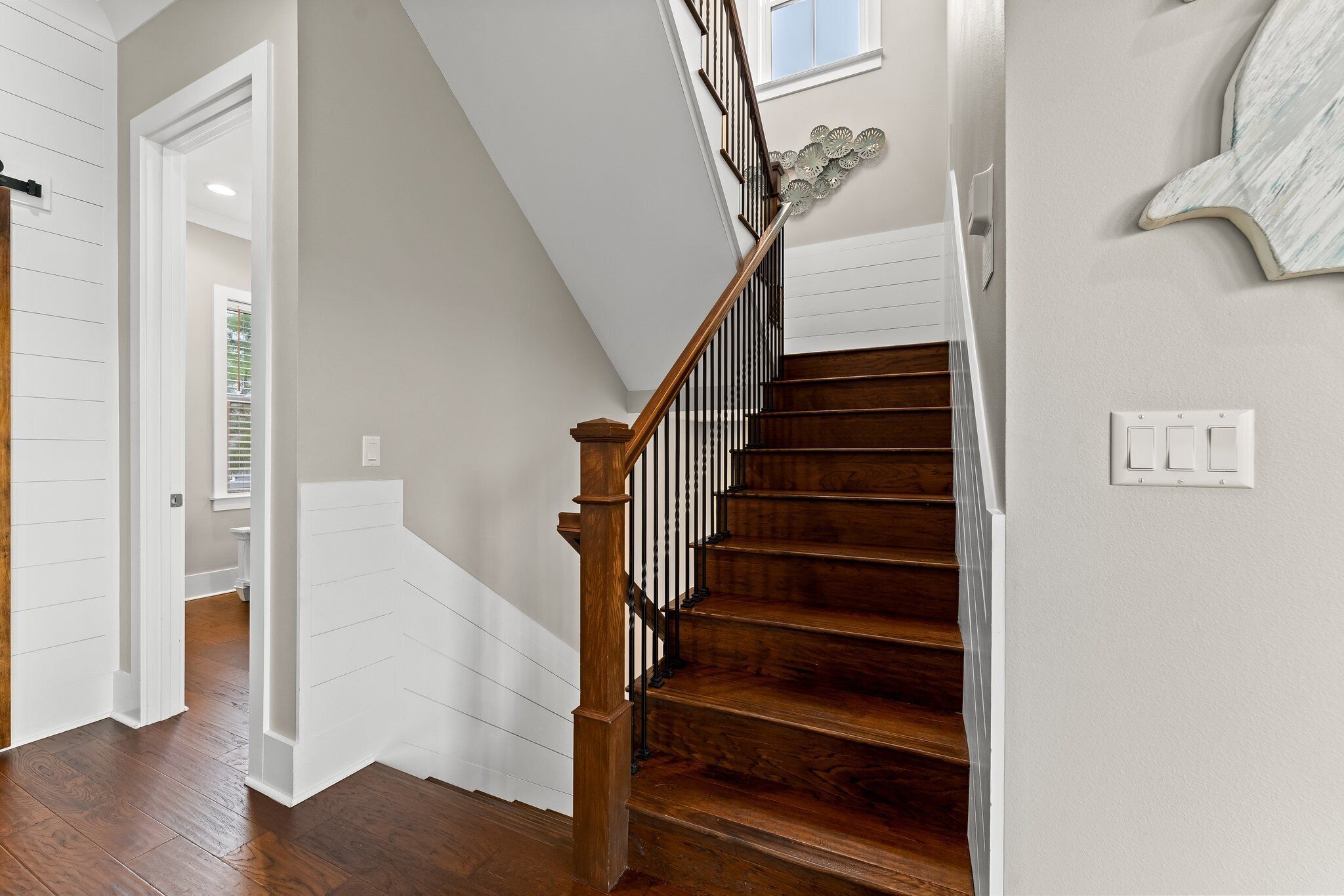 A wooden staircase with a white railing and a wall-mounted light switch.