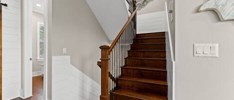 A wooden staircase with a white railing and a wall-mounted light switch.