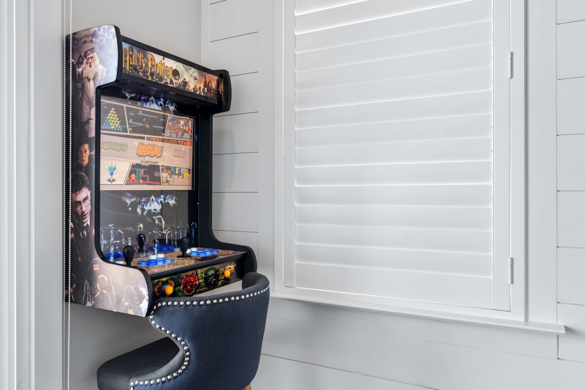 A retro arcade machine with a Harry Potter theme, a black chair, and a window with white blinds.