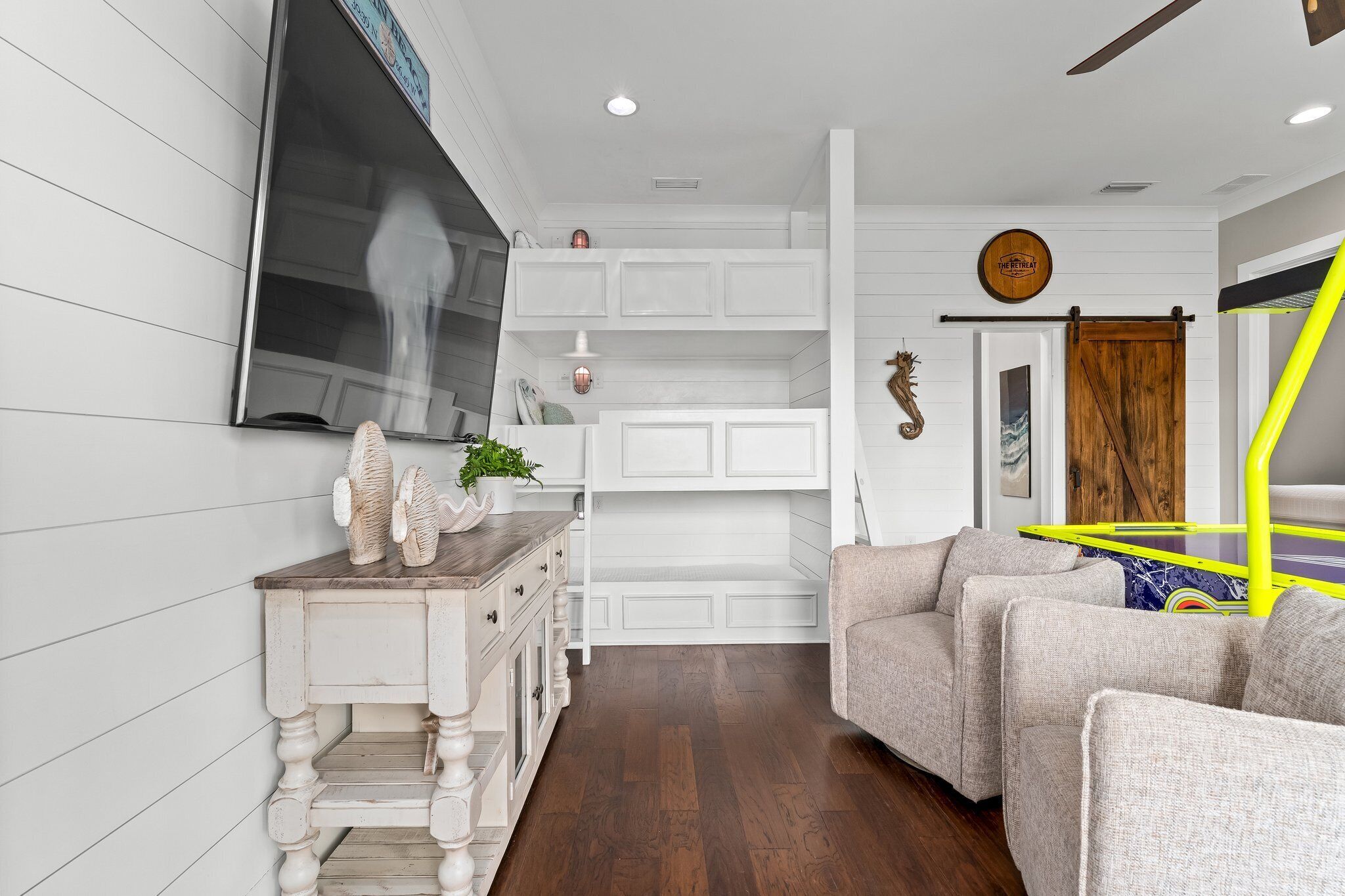 A modern living room with a white built-in bench, a TV mounted on the wall, and a yellow and blue play structure.
