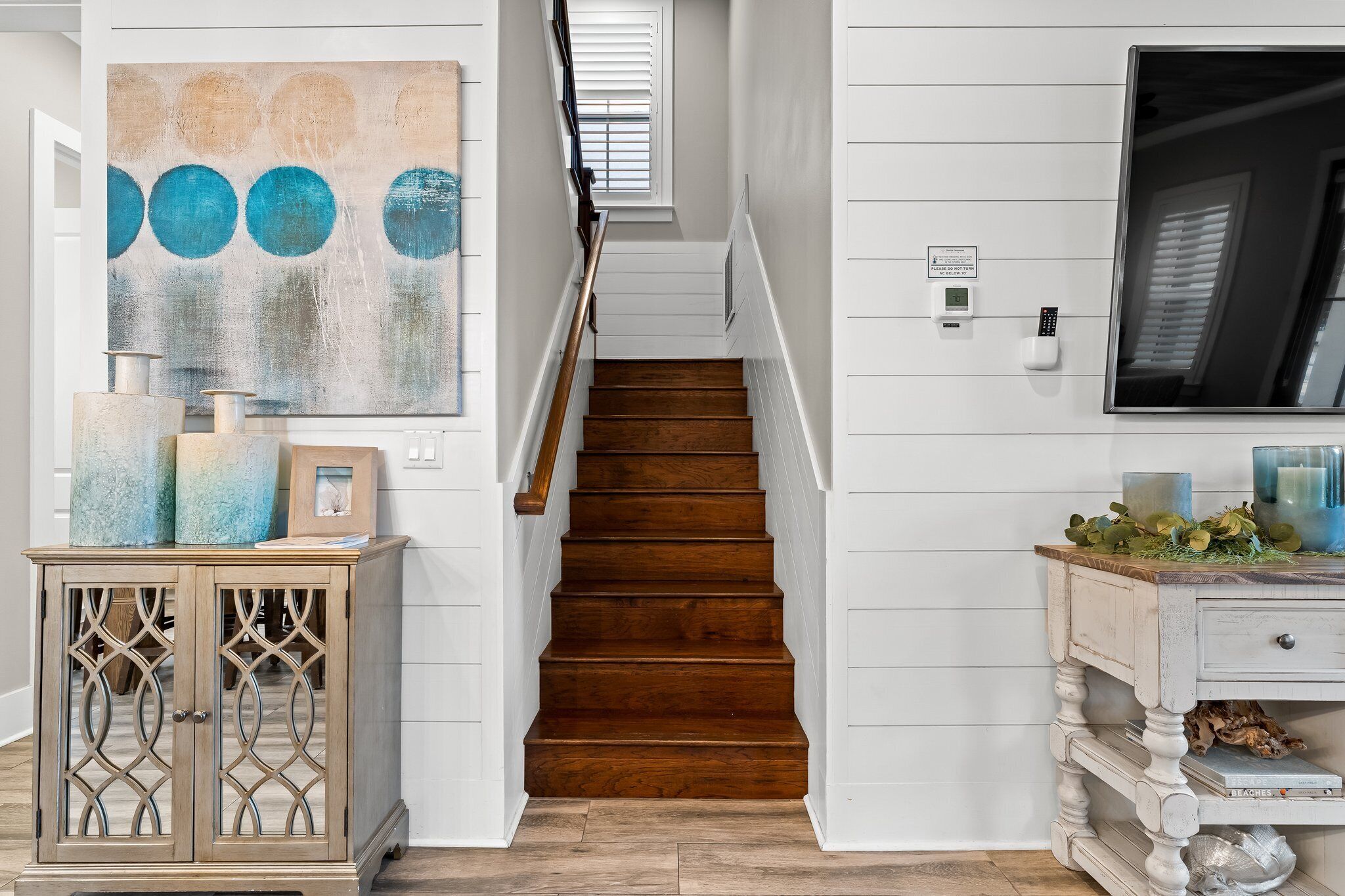 A staircase with wooden steps and white walls, a decorative cabinet with glass doors, and a painting with blue circles.
