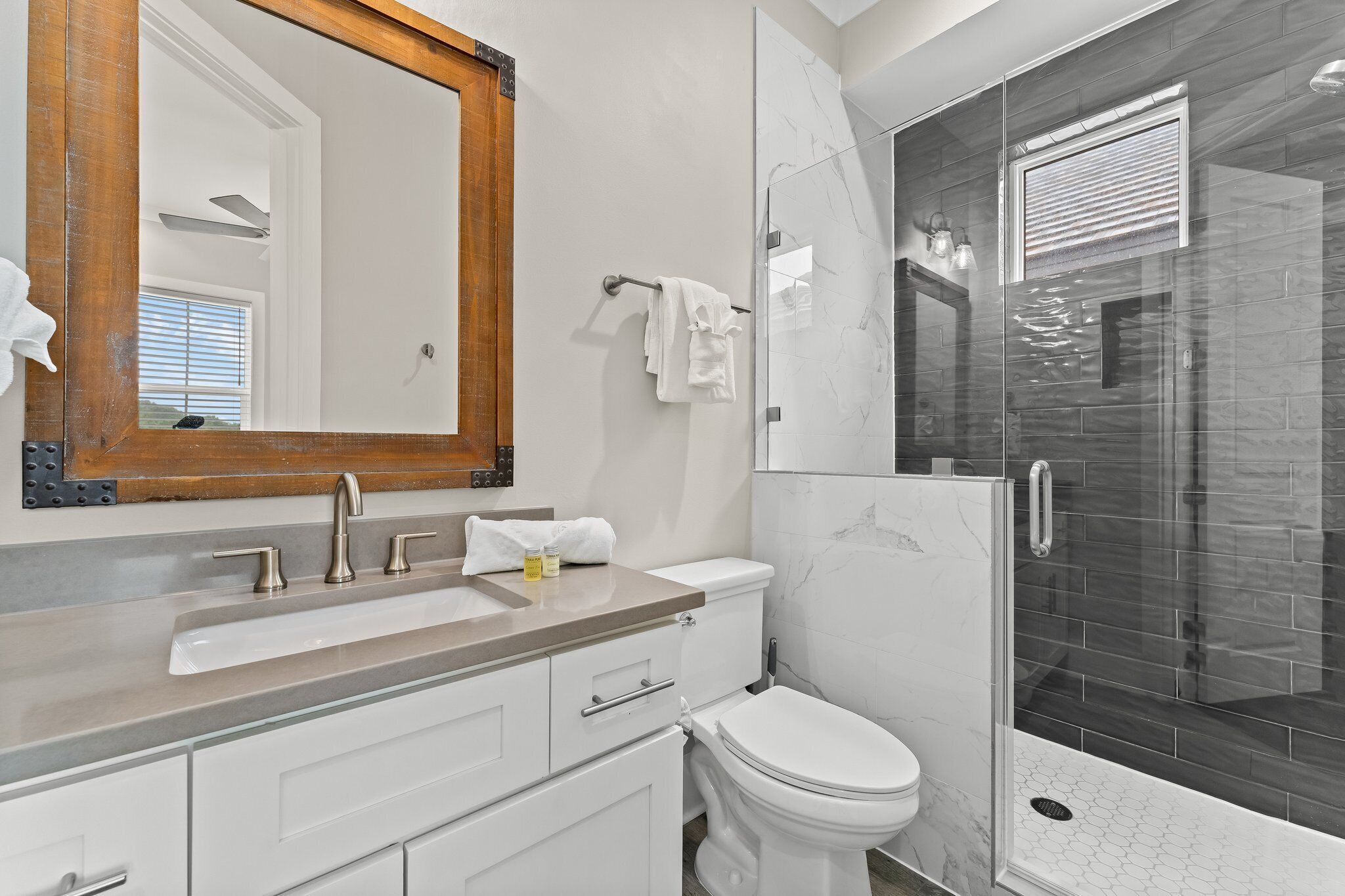 A modern bathroom with a large mirror, a sink, a toilet, and a glass-enclosed shower.