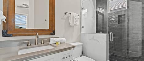 A modern bathroom with a large mirror, a sink, a toilet, and a glass-enclosed shower.