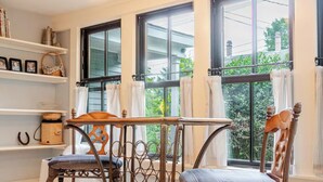 Una habitació amb una cadira i taula de fusta, una prestatgeria amb llibres i un búl, i finestres grans amb cortines.
