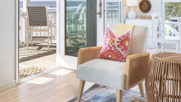 A room with a view of the ocean, a wicker chair, a rattan side table, and a white lamp.