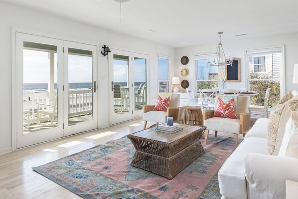 Un salón amplio con un gran ventanal corredera que da a un balcón, un sofá blanco, una mesa de centro y vistas a la playa.