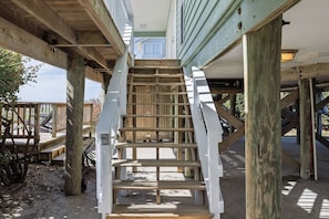Una escalera de madera conduce a un espacio al aire libre cubierto, con vista a una casa al fondo.