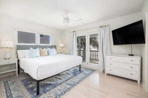 A bedroom with a bed, nightstands, a TV, a dresser, and a view of the outdoors.