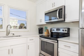 A modern kitchen with white cabinetry, a stainless steel refrigerator, a microwave, an oven, and a coffee maker.