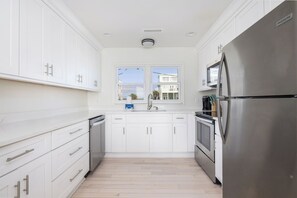 Una cocina moderna con armarios blancos, electrodomésticos de acero inoxidable y una ventana con vistas a edificios.