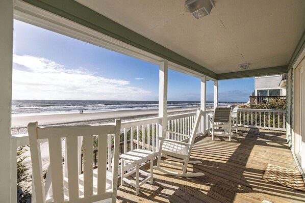 A wooden deck with white railings overlooking a beach.